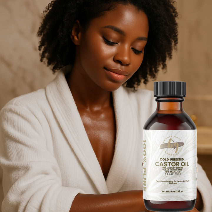 An African American woman in a white bathrobe looking down at a bottle of cold-pressed castor oil.