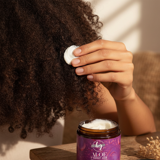 Woman applying a Aloe and Carrot Seed Moisturizing Hair Cream to their hair with a jar of it on a table.